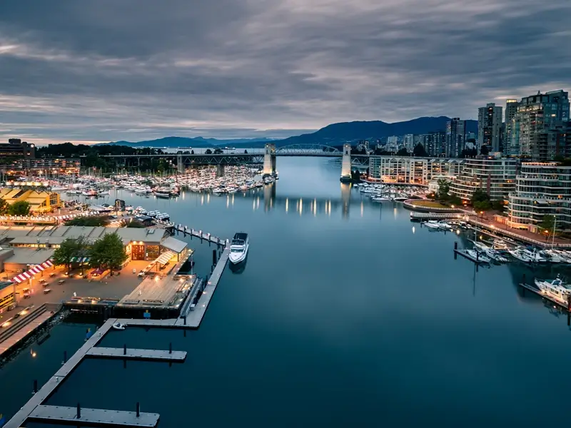 City harbor at dusk with boats, bridges, and waterfront buildings.