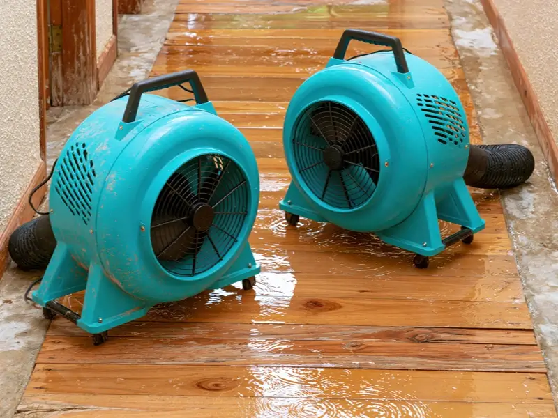 Two turquoise floor fans drying a wet wooden floor.